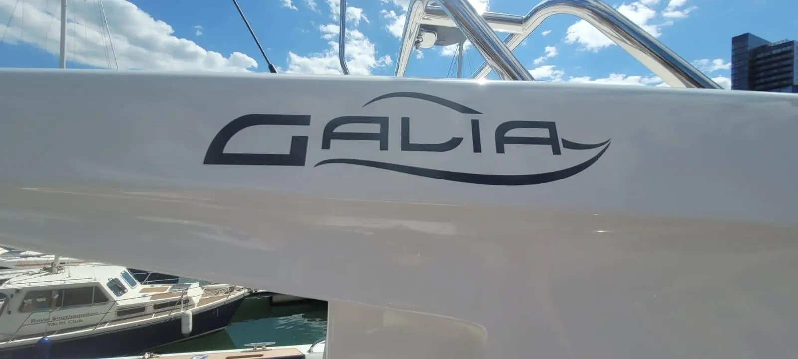 Galia logo displayed on the side of a boat with a blue sky and clouds in the background at a marina.